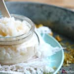 Sugar scrub with a popsicle stick in a small glass jar placed on top of a white cloth