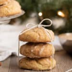 Stack of three gluten-free egg nog cookies tied by a thin white ribbon and a plate of the same cookies behind it