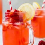 Close up of a mason glass jar of sugar-free strawberry lemonade with a slice of lemon and a red and white striped straw