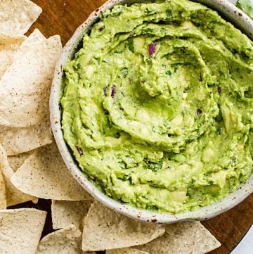 guacamole in a bowl with some tortilla chips surrounding it