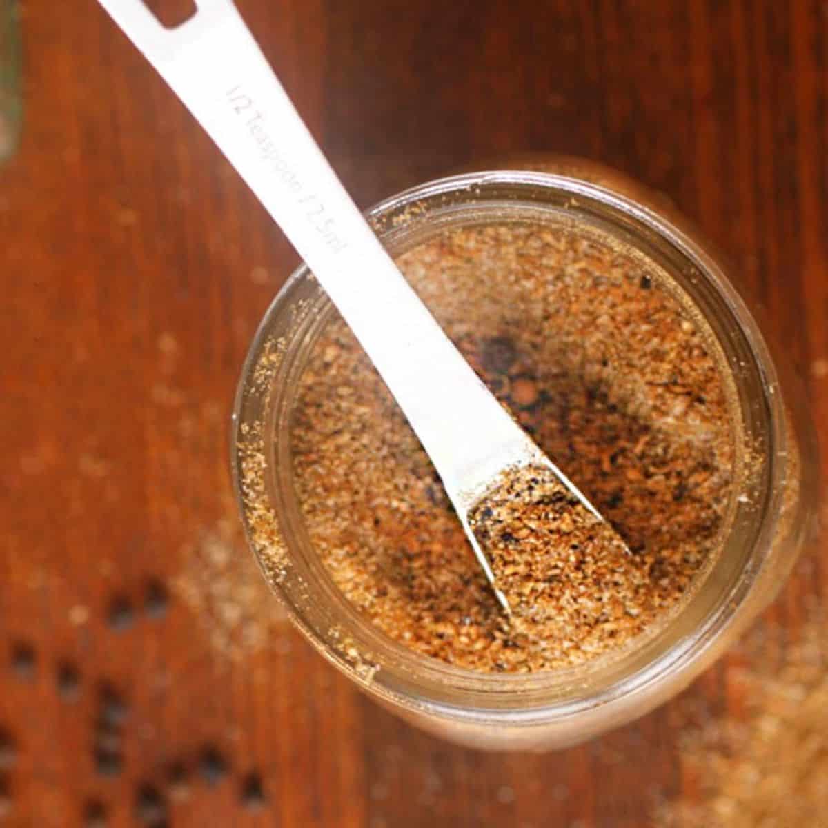 chaat masala in glass jar with measuring spoon.