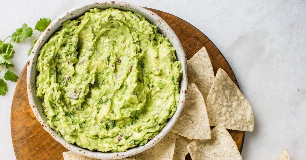 guacamole in a bowl with chips on the side.