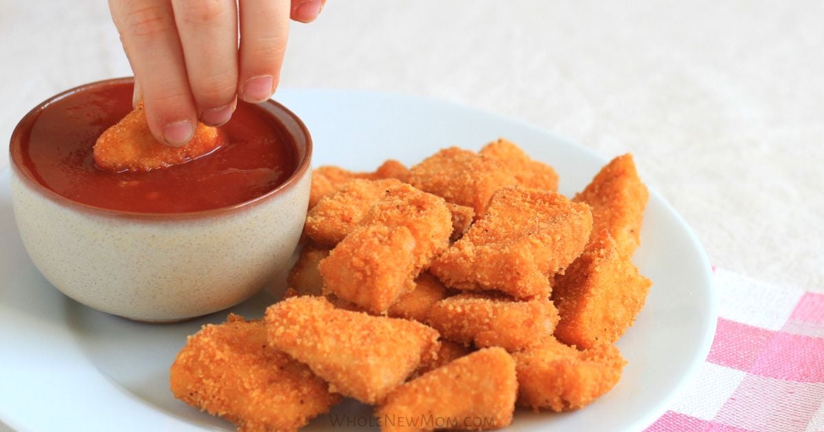 plate full of chicken nuggets and a nugget dipped in ketchup.