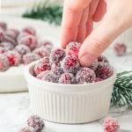 hand picking up a cranberry from a small white ramekin of healthy candied cranberries.