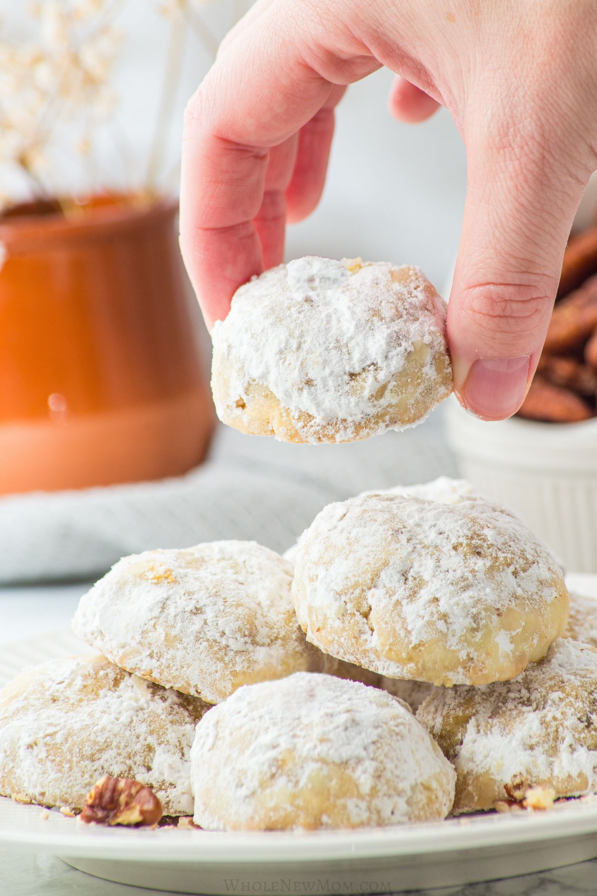 hand picking a cookie off of a plate of keto snowball cookies.
