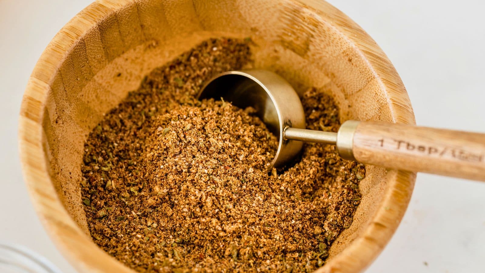 homemade taco seasoning in small wooden bowl with gold measuring spoon with wood handle.
