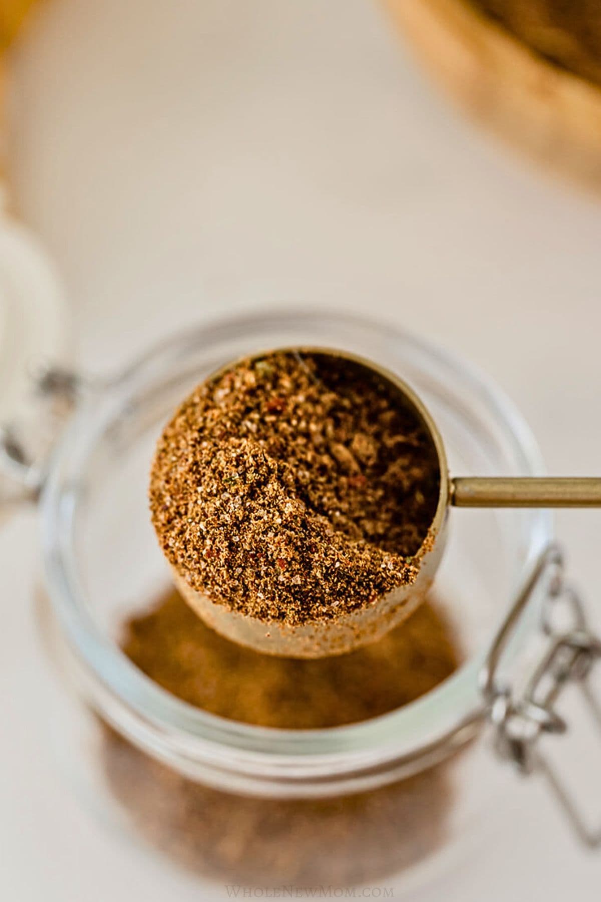 gold measuring spoon putting homemade taco seasoning into a glass jar.