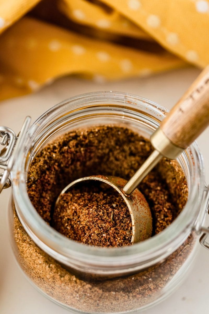 homemade taco seasoning in a glass jar with a gold measuring spoon.