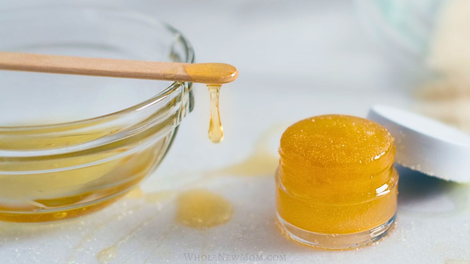 diy honey lip scrub in a jar next to glass bowl of honey with honey dripping from wooden stick.