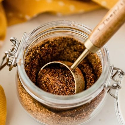 homemade taco seasoning in a jar with a gold measuring spoon with a wooden handle.