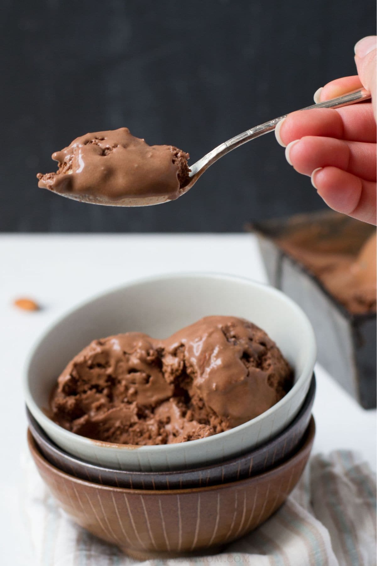 hand holding a spoon of chocolate almond chip ice cream.