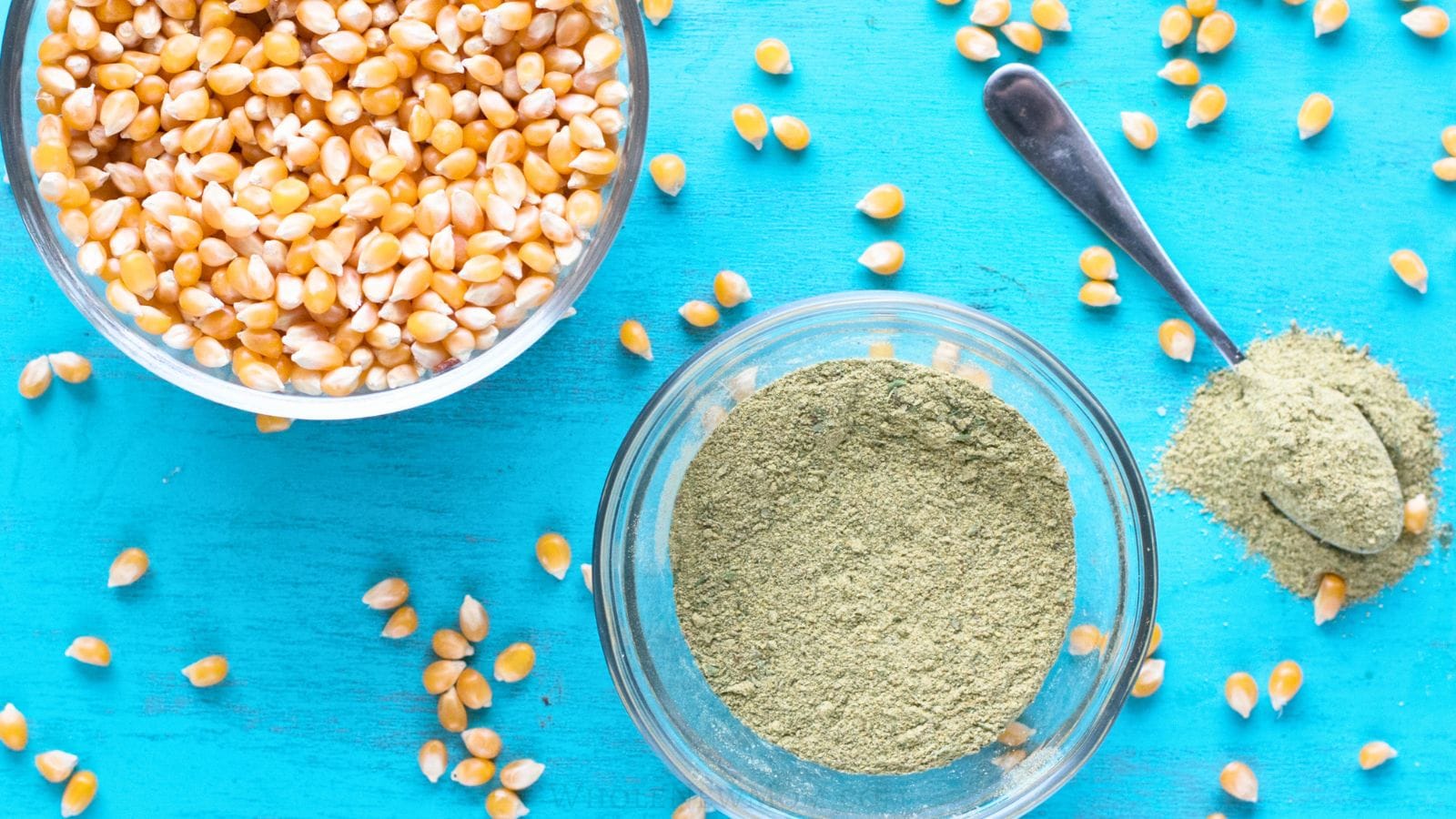 homemade popcorn seasoning in glass bowl and on spoon with popcorn kernels.