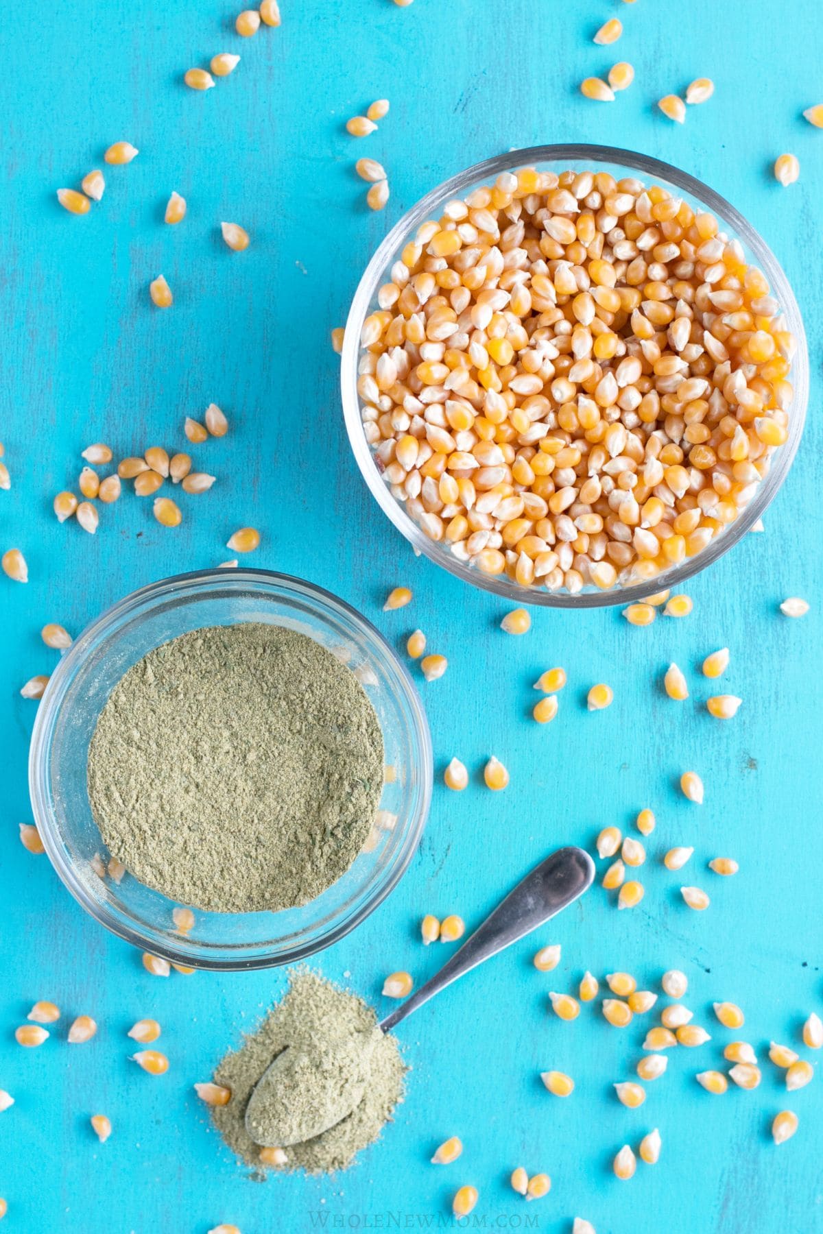 homemade popcorn seasoning in small glass bowl and on spoon with popcorn kernels.