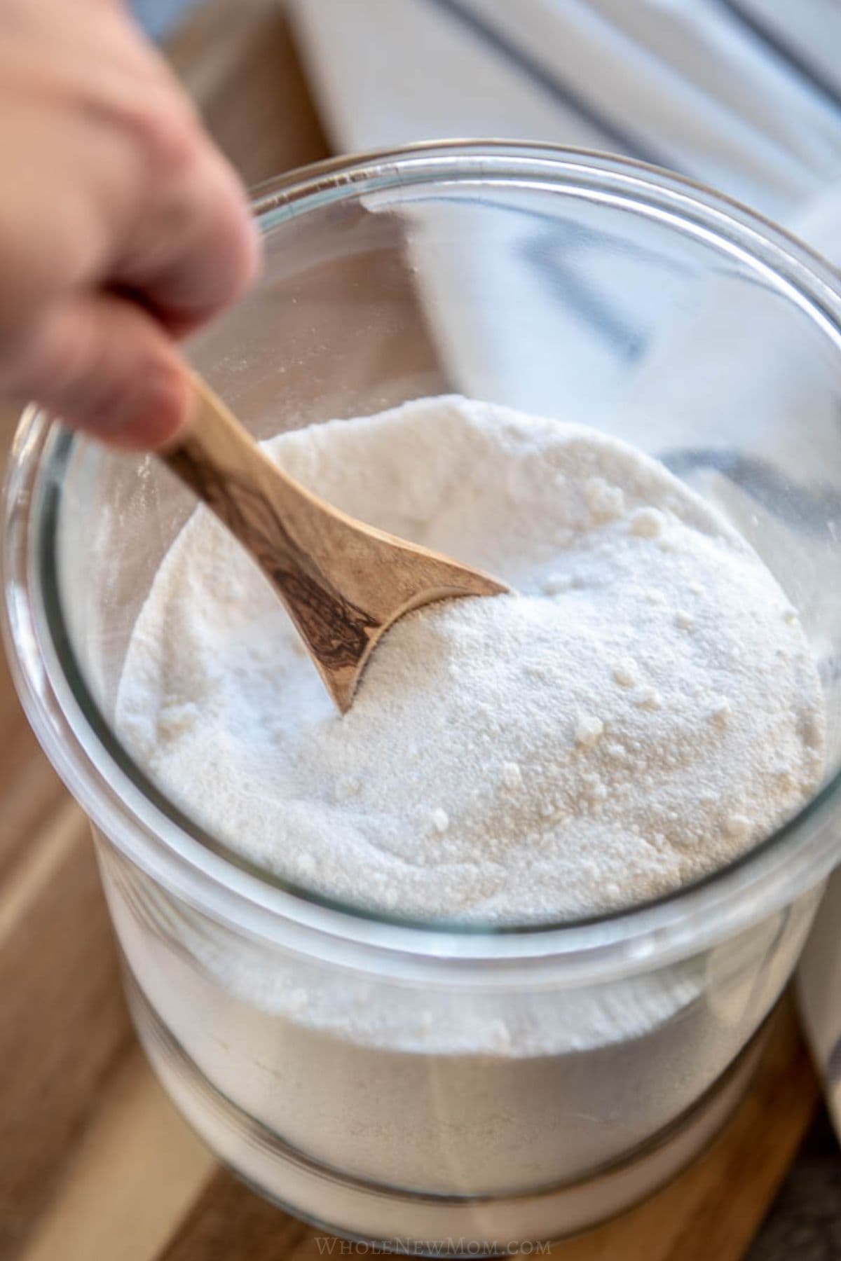 hand stirring non-toxic homemade laundry detergent in jar with wooden spoon.