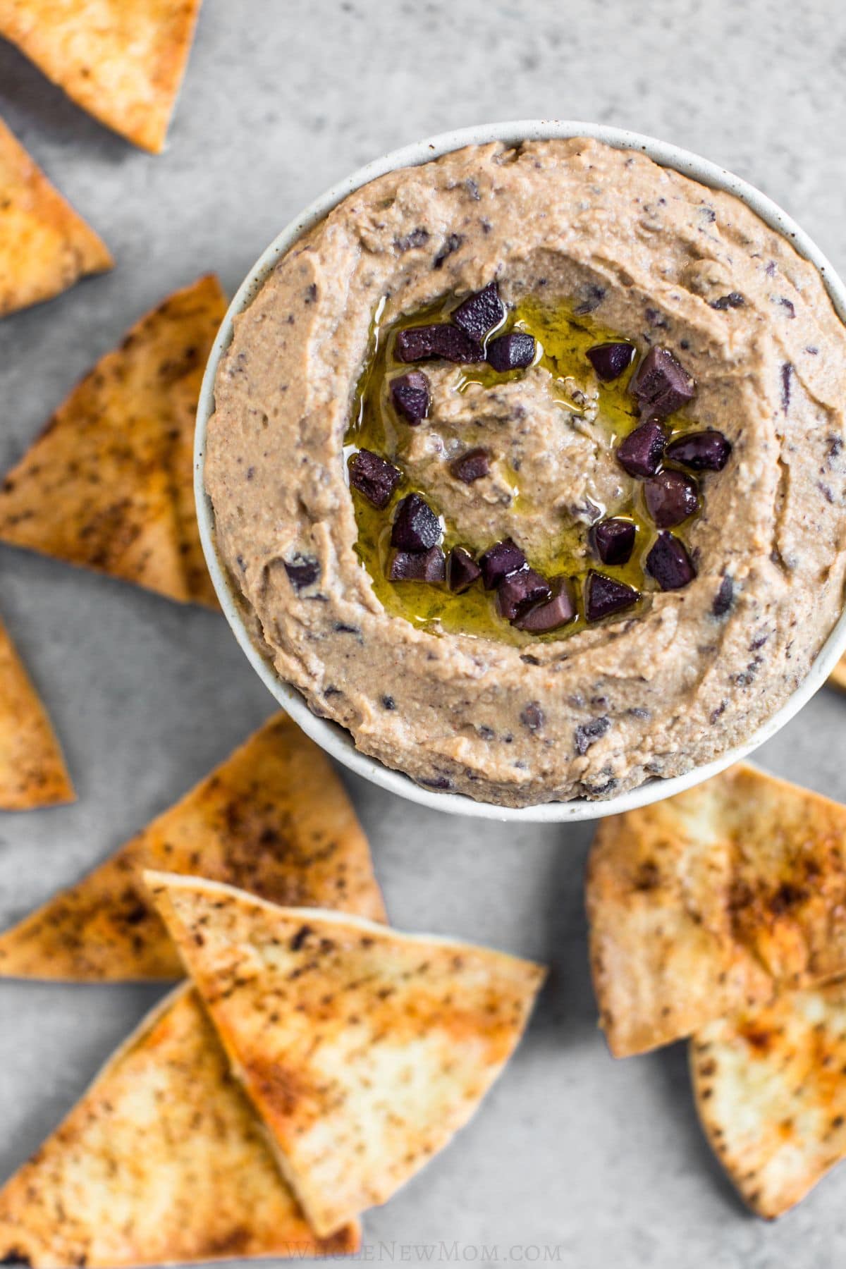 olive hummus in bowl with pita wedges scattered around it.