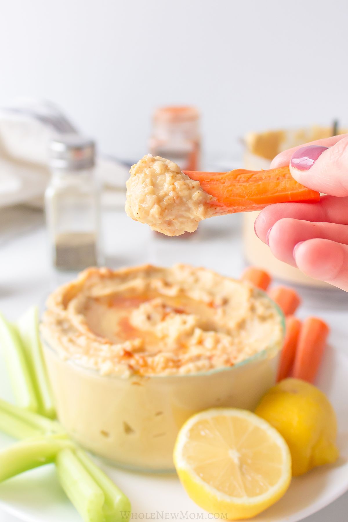 hand holding carrot stick dipped in sesame-free hummus.