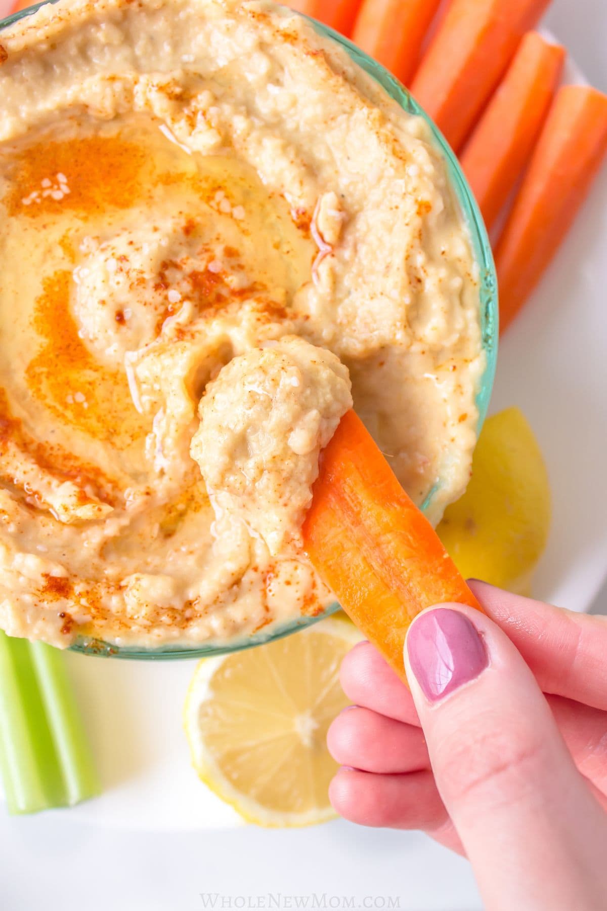 hand dipping carrot stick into sesame-free hummus.