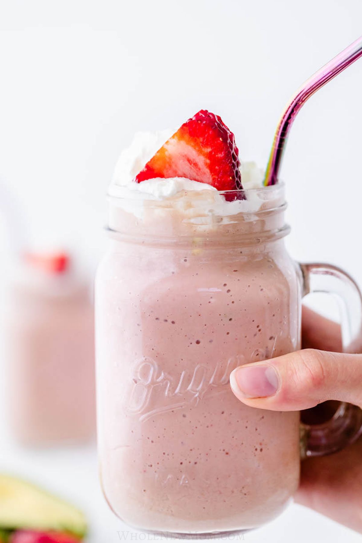 hand holding strawberry avocado smoothie in mason jar mug.