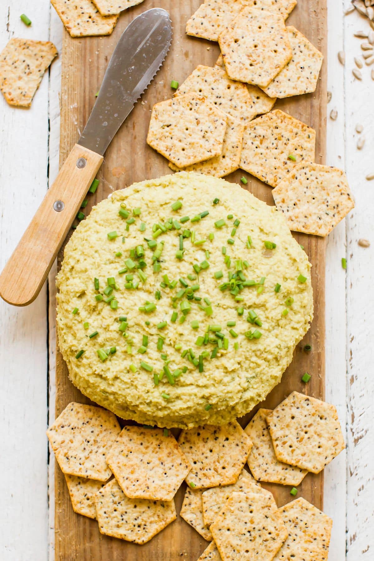 sunflower seed cheese with gluten-free crackers on wood cutting board.