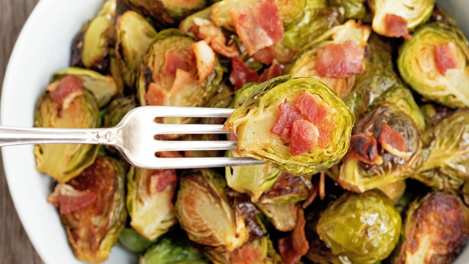 roasted brussels sprouts with bacon on a fork showing crispy edges.