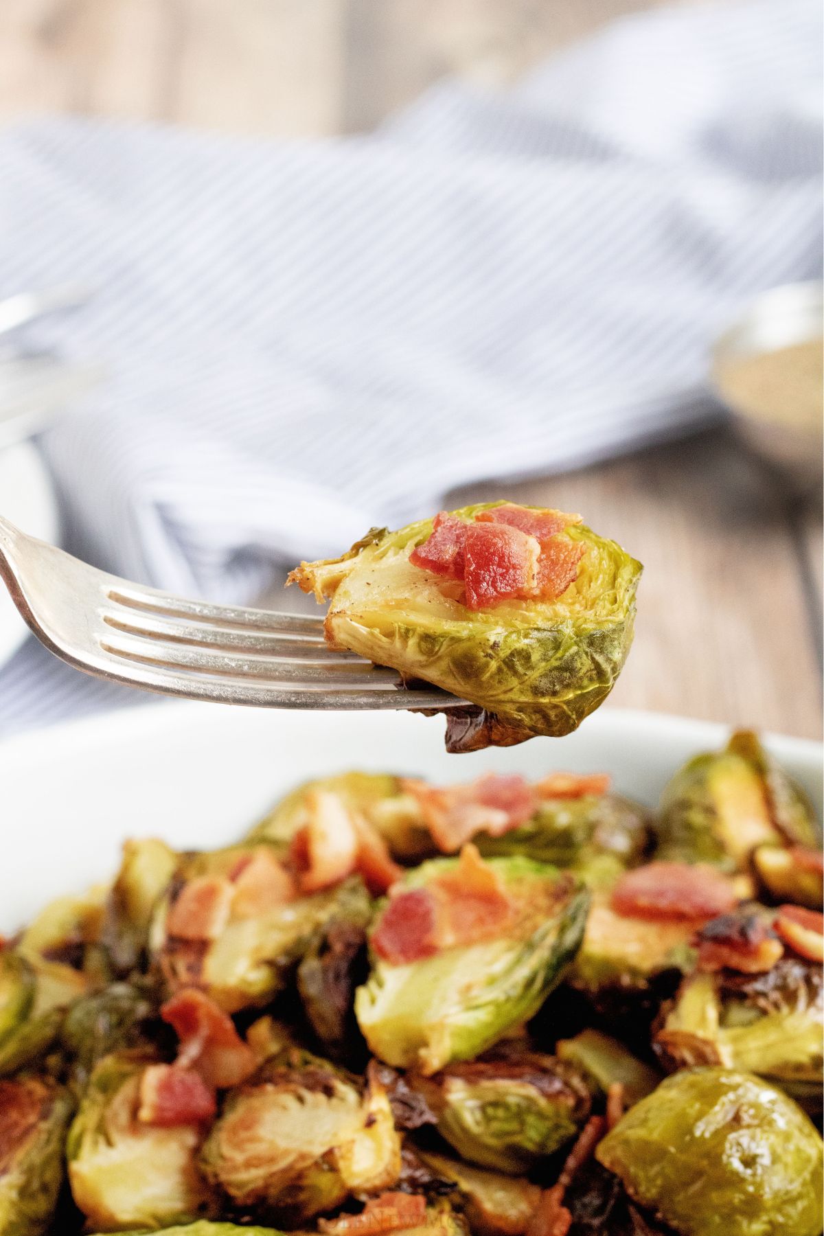 fork holding roasted brussels sprout with bacon over bowl of roasted brussels sprouts.