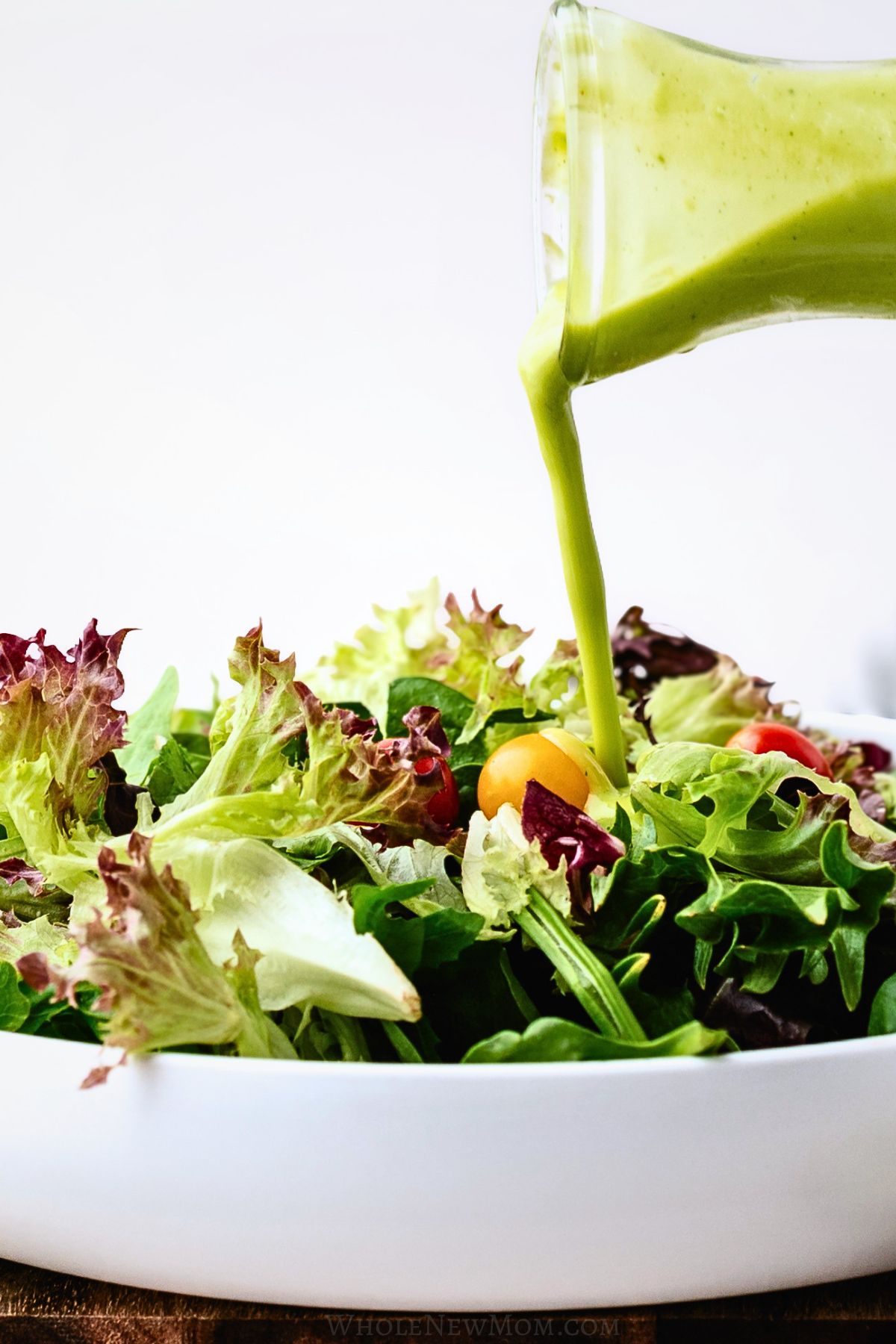 dairy free avocado dressing being poured on salad in white bowl.