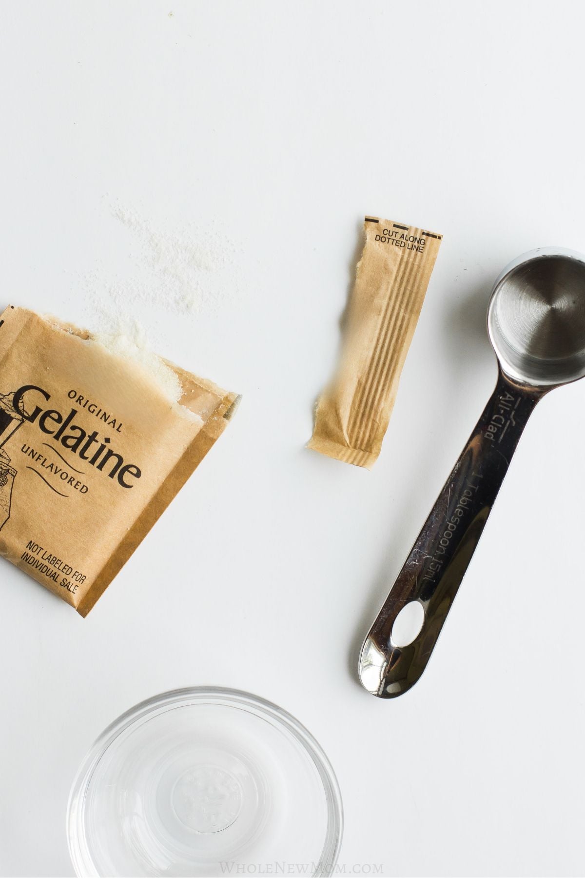 opened gelatin packet with measuring spoon and small glass bowl.
