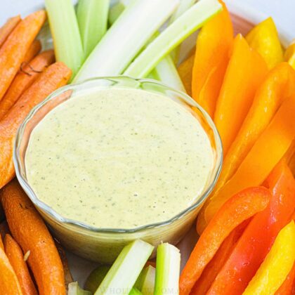 vegan ranch dressing in small glass bowl surrounded by vegetable sticks.