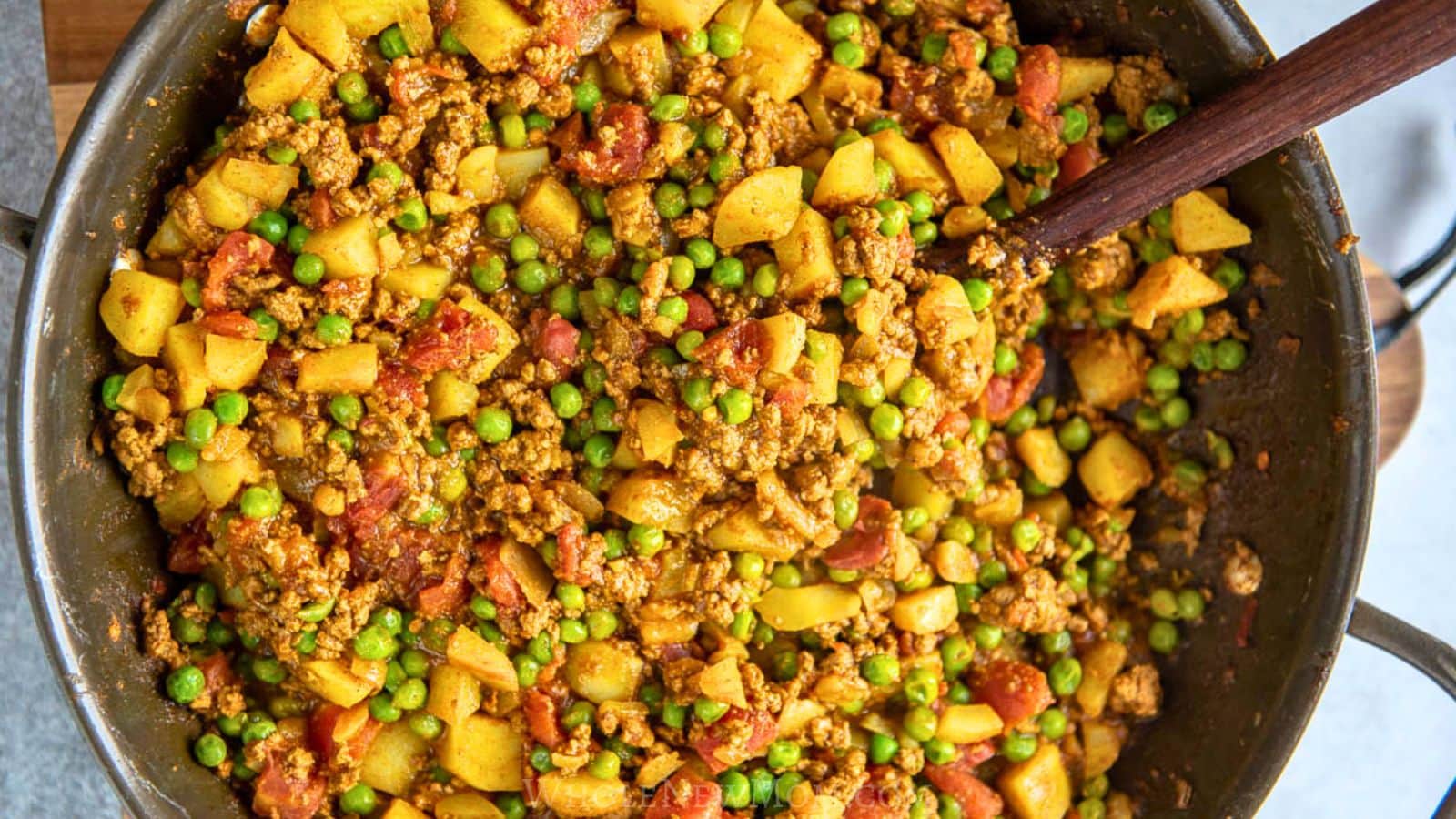 Pakistani keema curry with ground beef, peas, and potatoes in skillet.