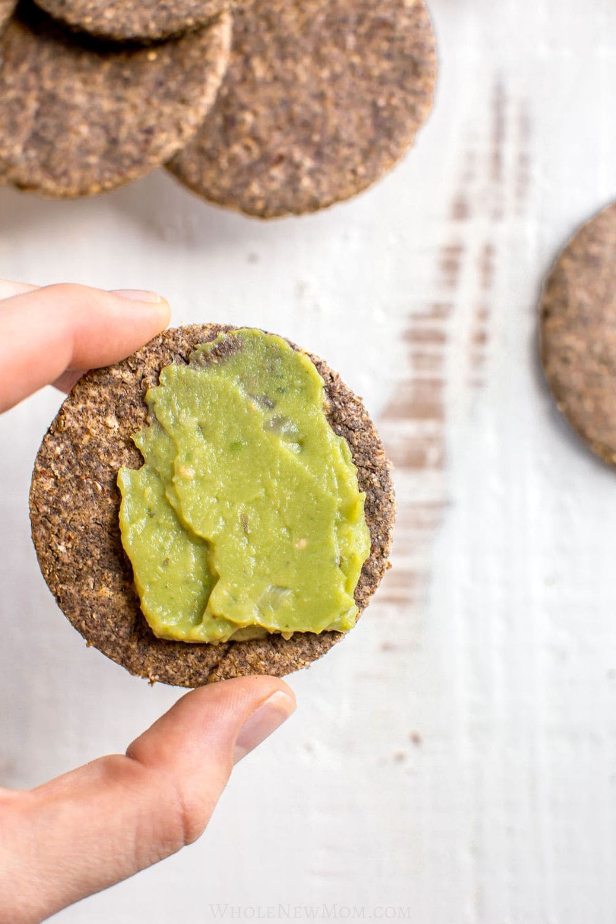 hand holding lentil cracker with guacamole spread on it.
