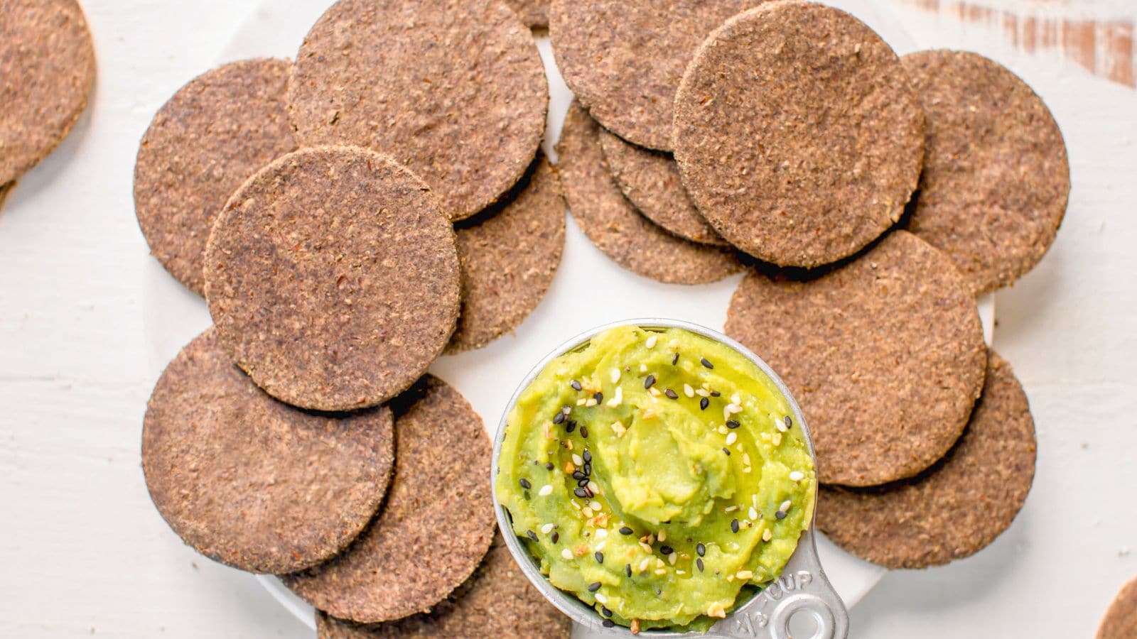 lentil crackers on white plate with small measuring cup with guacamole and everything seasoning.