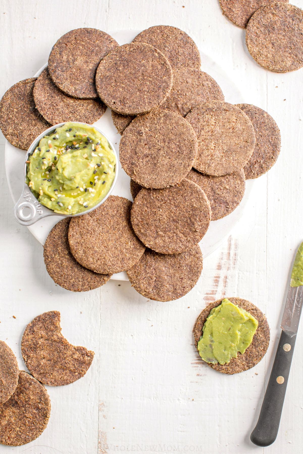 lentil crackers with small cup of guacamole on white plate and cracker with guacamole spread on it.