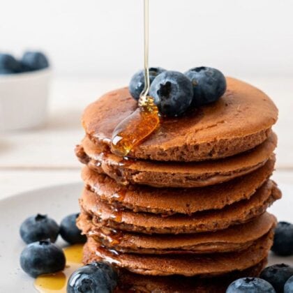 maple syrup being poured on teff pancakes with blueberries.