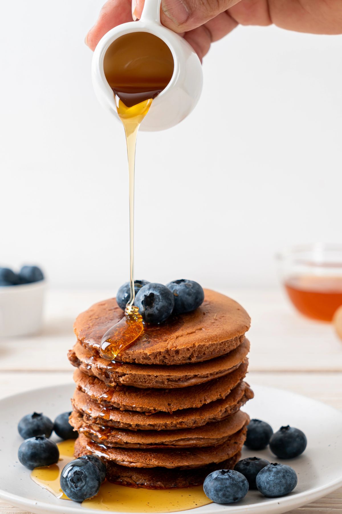 pouring syrup on teff pancakes with blueberries.