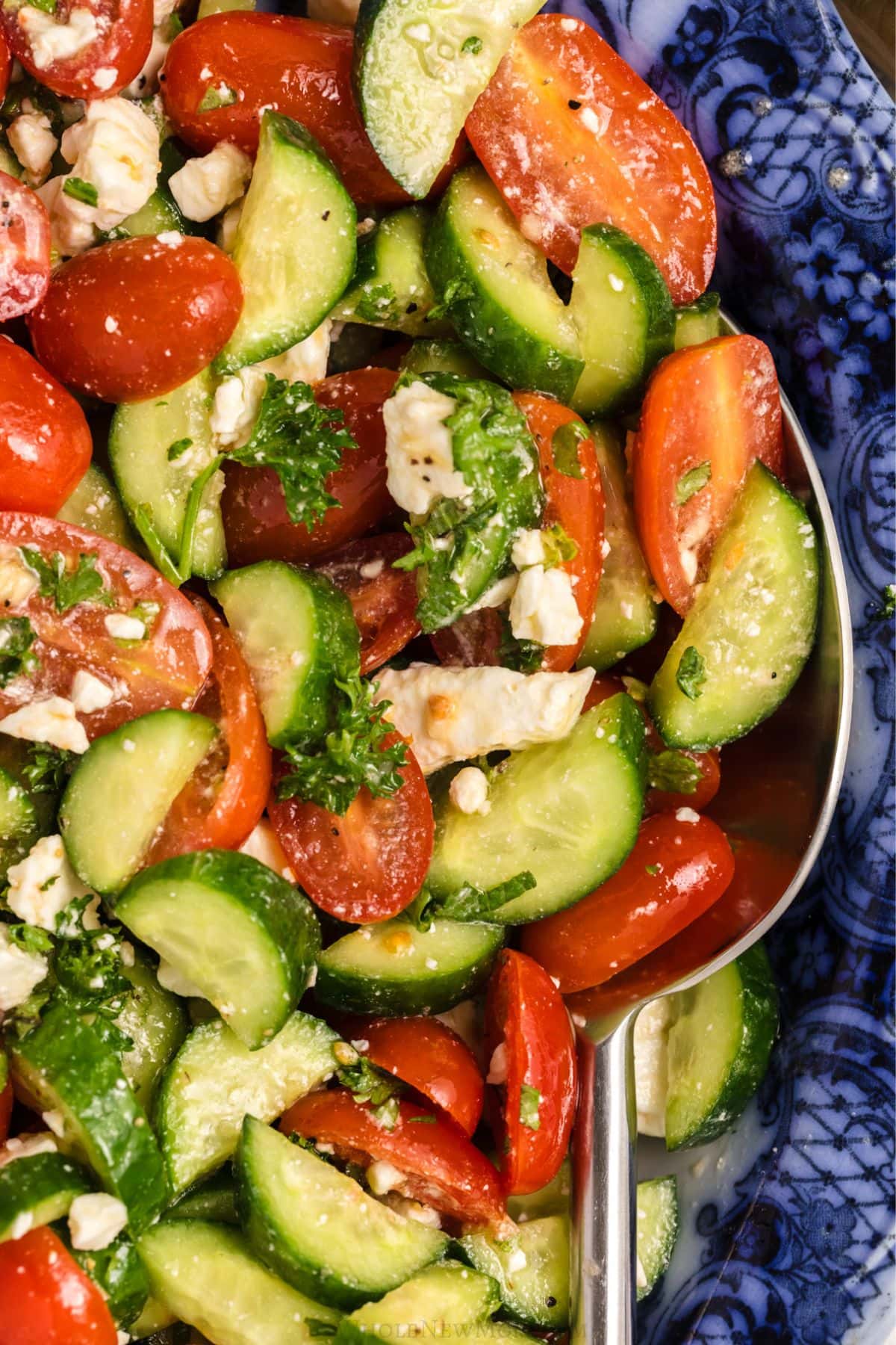 Salad being scooped with a spoon from a blue dish.