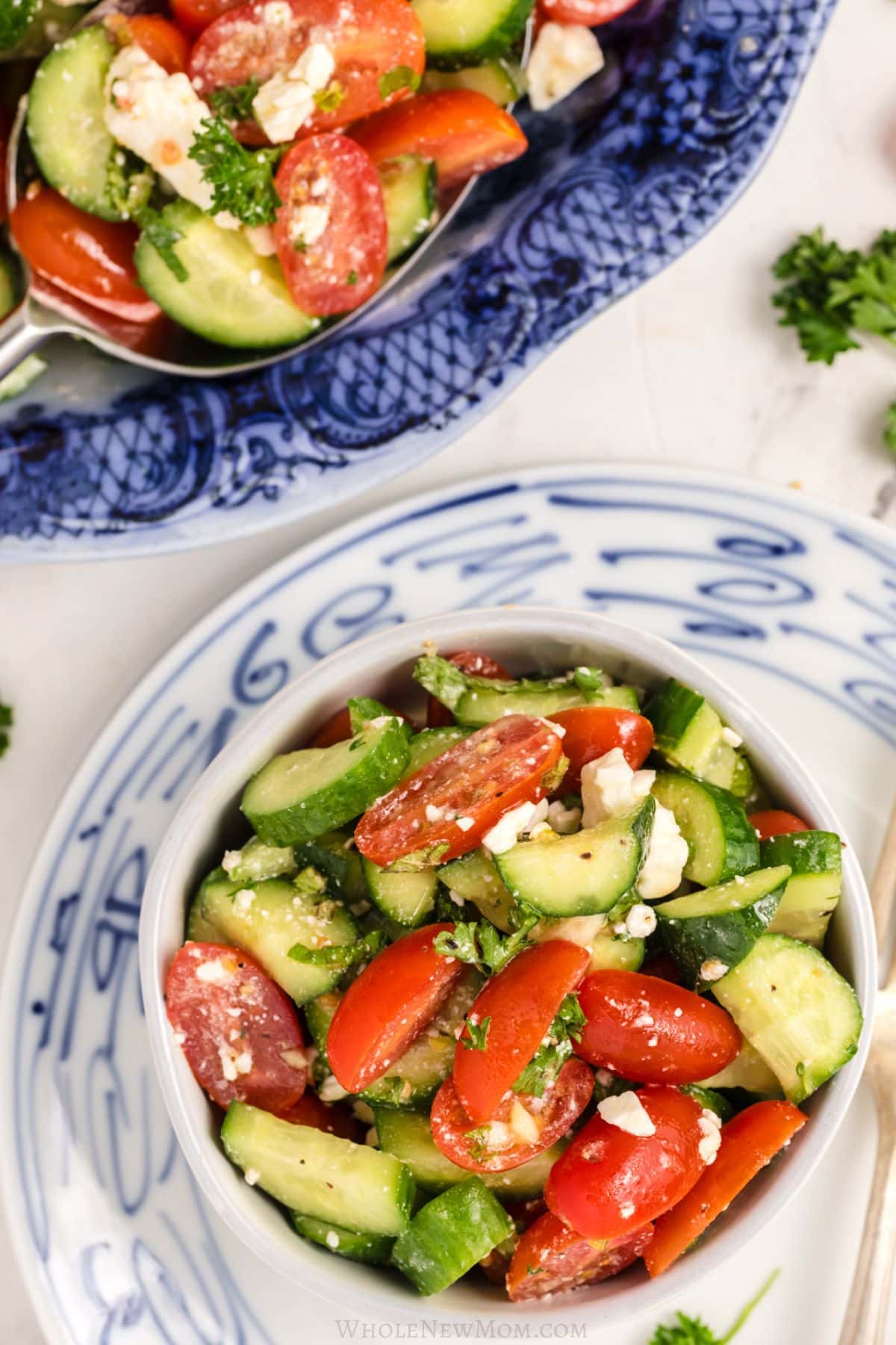 A small white bowl of salad placed below a larger blue serving platter.