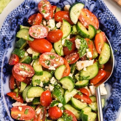 A salad tossed with herbs, served in a blue serving dish with a spoon.
