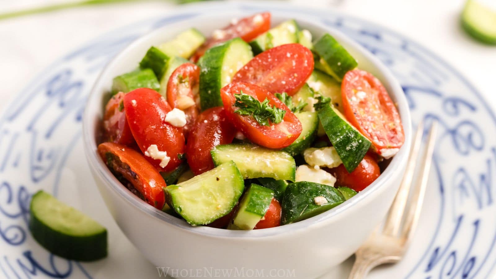 A white bowl filled with salad, set on a plate with fork.